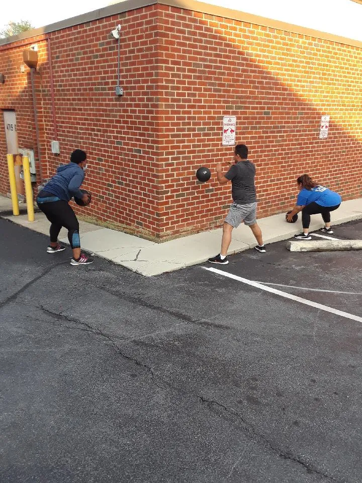 Members throwing medicine balls against the brick wall outside the gym